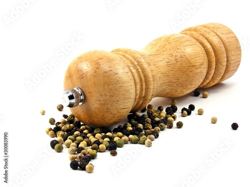 A wooden peppermill with peppercorns on white background