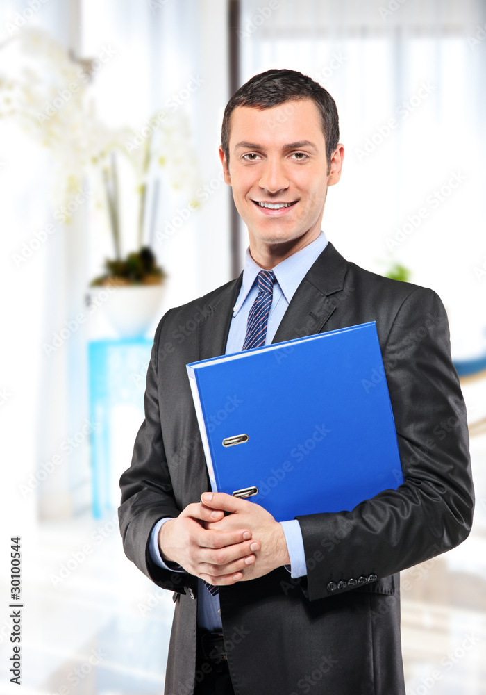 Happy businessman with blue folder posing in the office Happy businessman with blue folder posing in the office