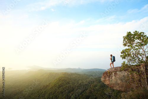 Young woman with a backpack standing on cliff s edge and looking to somewhere