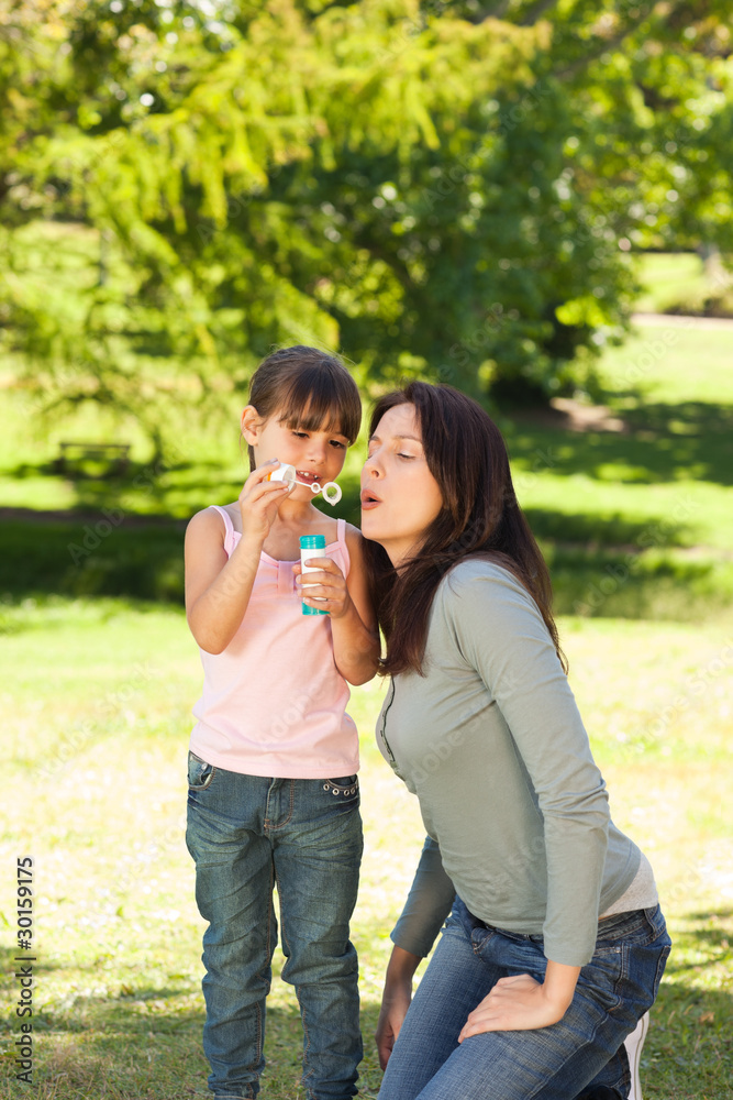 Girl blowing bubbles with her mother in the park Girl blowing bubbles with her mother in the park