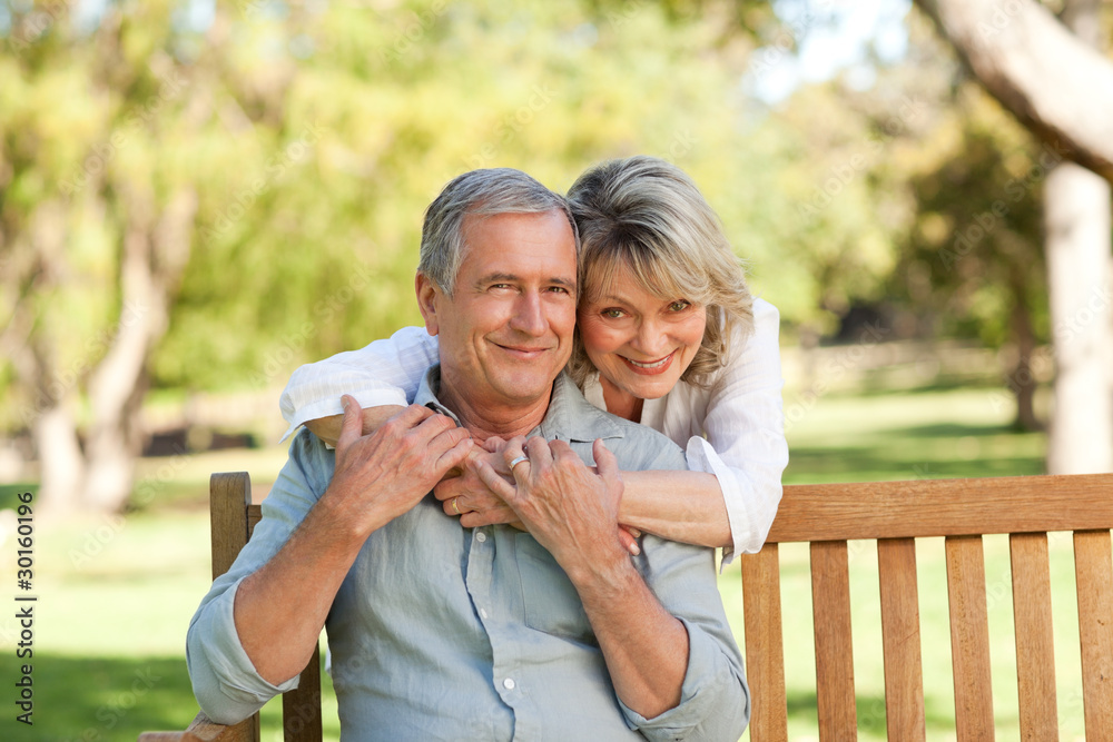 Naklejka premium Senior woman hugging her husband who is on the bench
