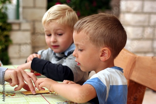 Two boys play board game, looking to hand with a card