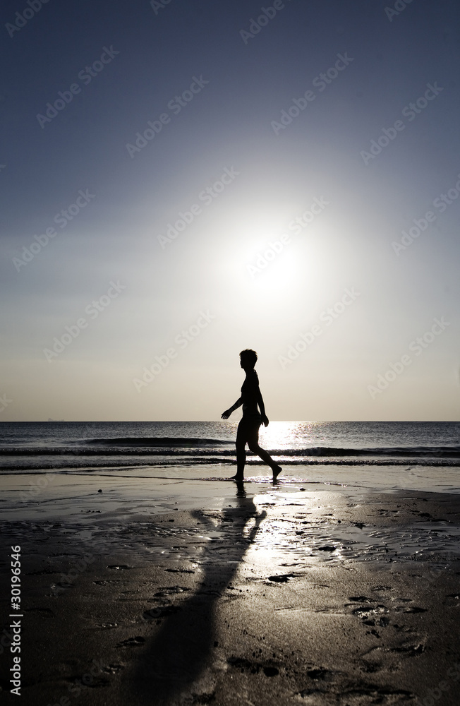 Fototapeta premium Woman strolling on the beach at sunset