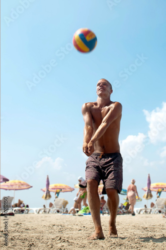 young man playing volleyball on a beach.