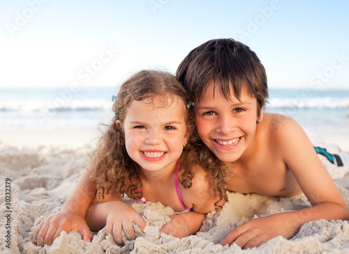 Little boy and his sister lying down on the beach photo