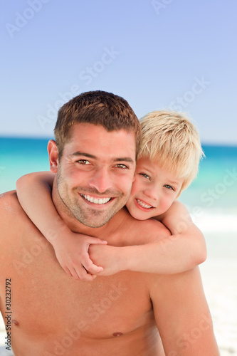 Smiling father having son a piggyback at the beach