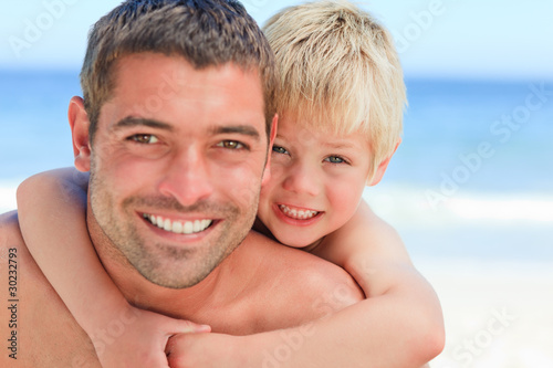 Smiling father having son a piggyback at the beach