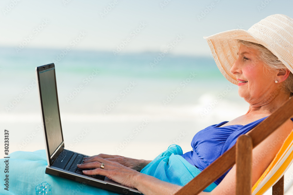 Happy woman working on her laptop at the beach