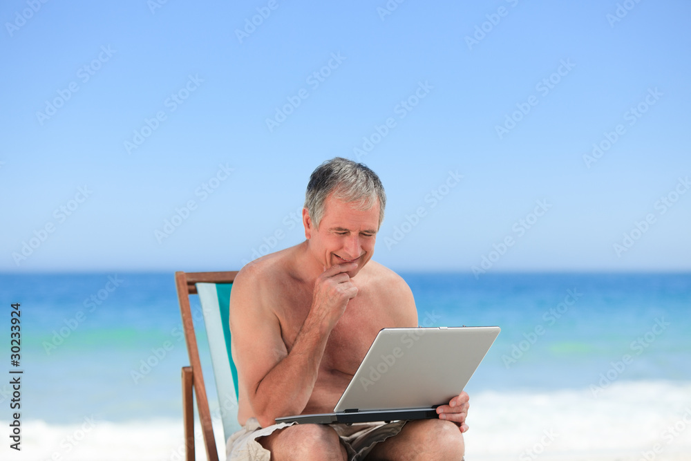 Retired man working on his laptop on the beach