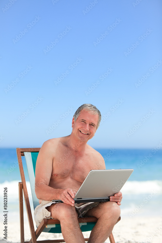 Retired man working on his laptop on the beach