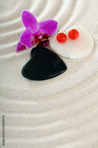 Steine als Herz im Sand mit Spuren und Blume