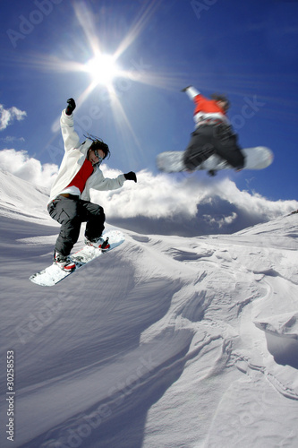 Snowboarders jumping against blue sky