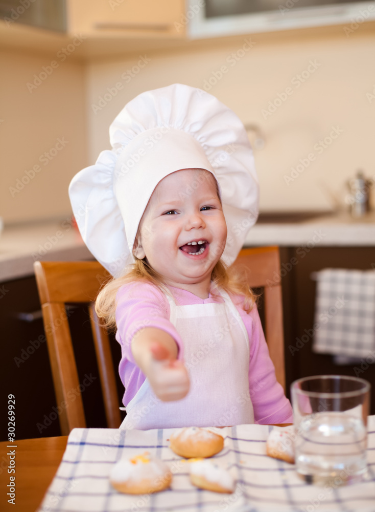 Happy little cook girl sitting at kitchen table with cookies and Happy little cook girl sitting at kitchen table with cookies and