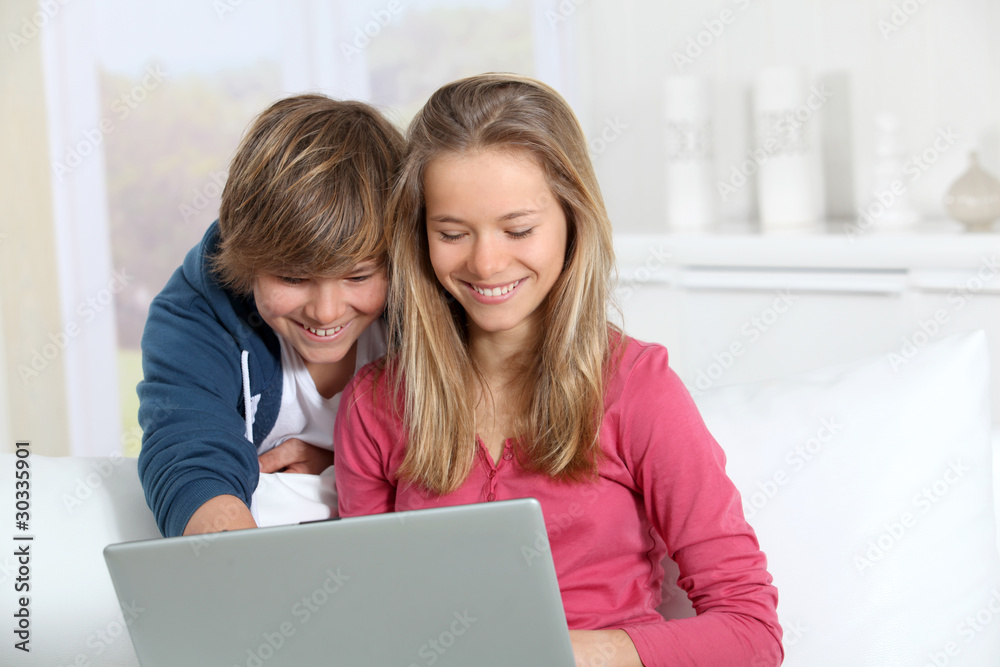 Brother and sister using laptop computer at home