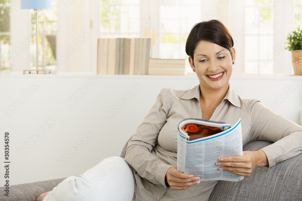 Happy woman reading newspaper on sofa Happy woman reading newspaper on sofa