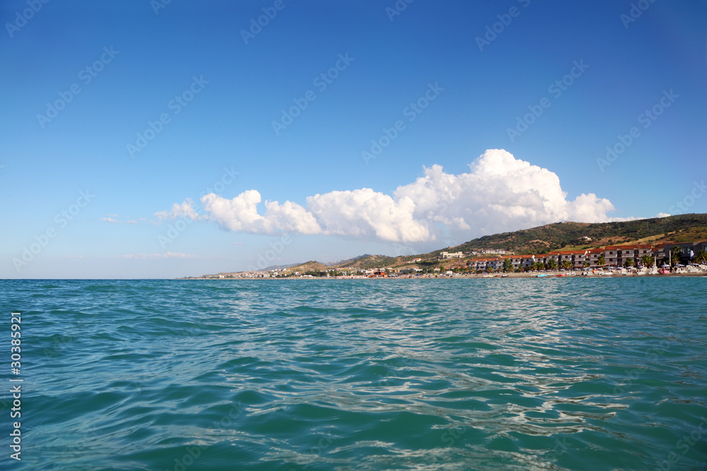 Naklejka premium blue water of sea, far away beach, mountains and building