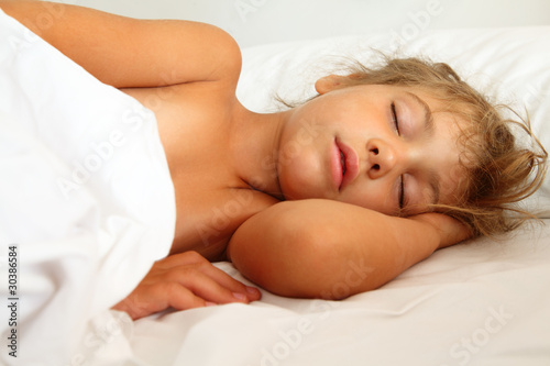 beautiful little girl asleep in bed on white sheet and pillow