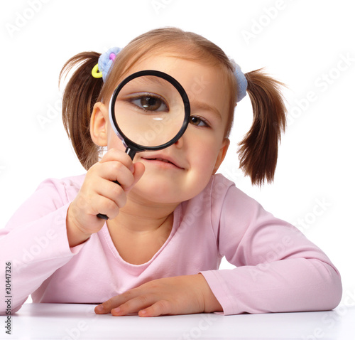 Curious girl is looking through magnifying glass