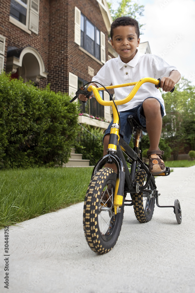 Young boy riding his first bicycle with training wheels Young boy riding his first bicycle with training wheels