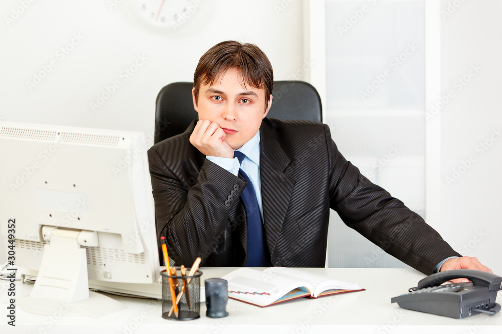 Thoughtful elegant business man sitting at desk in office.