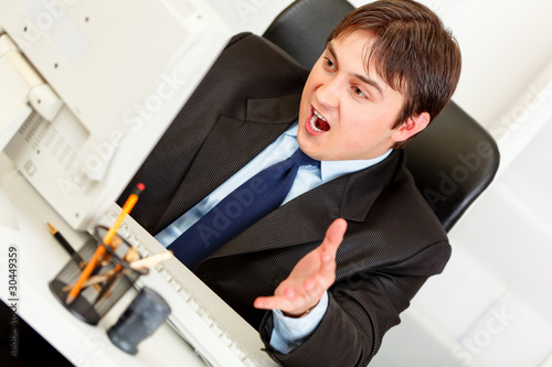 Stressful businessman sitting at desk and looking at monitor.