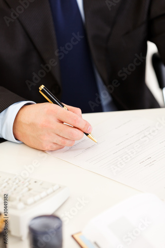 Businessman sitting at desk and signing protocol. Closeup.