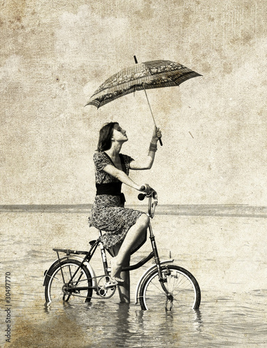 Girl with umbrella on bike. Photo in old image style.