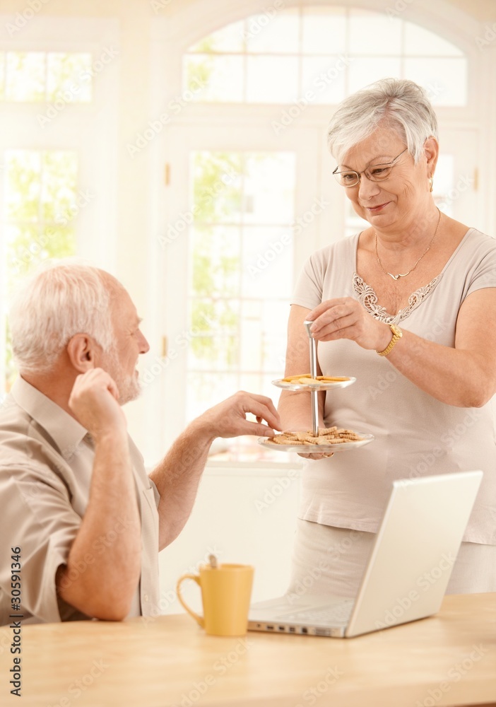 Smiling wife serving cookies in kitchen to husband