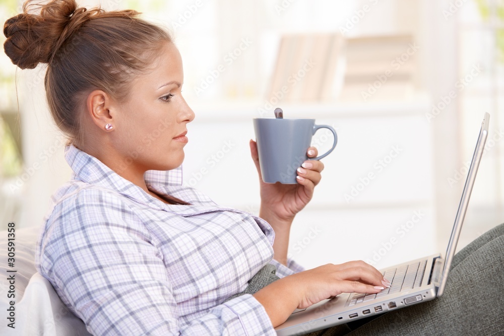 Young woman using laptop in bed drinking tea Young woman using laptop in bed drinking tea