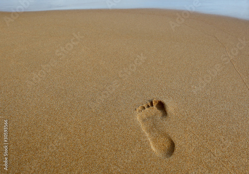 Footprint on a sandy beach with the ocean across the top of the frame.