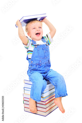 Cute little boy is sitting on a heap of textbooks