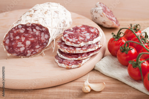 Traditional sliced salami on wooden board with garlic, cherry to