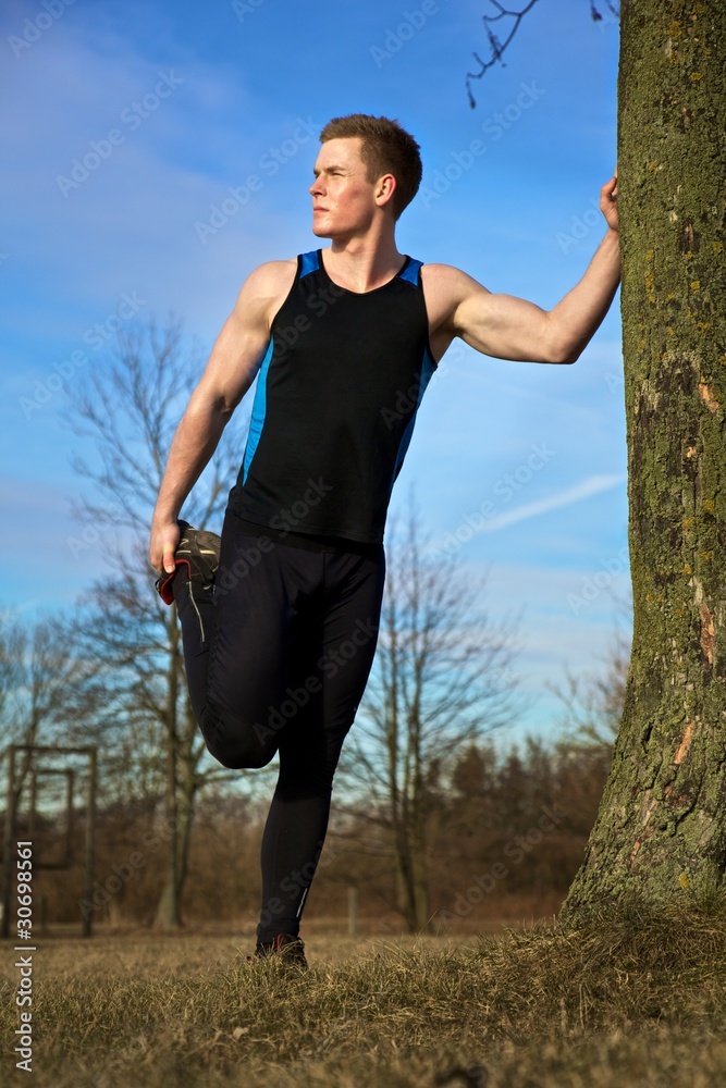 Young man stretching against tree after workout