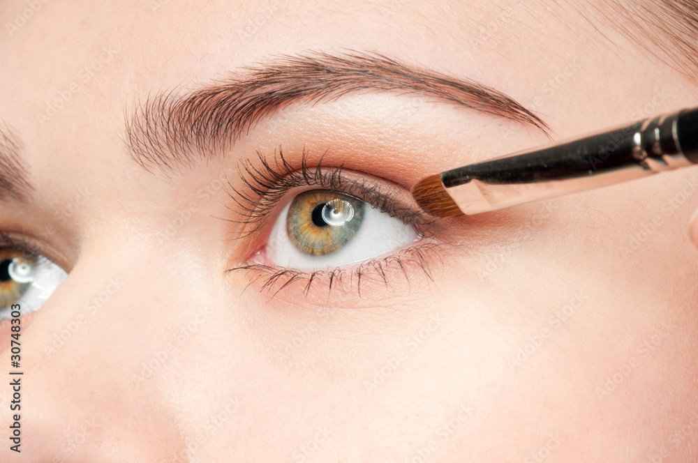 Naklejka premium Beautiful young adult woman applying cosmetic shadow brush