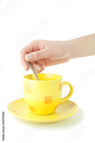 Yellow coffee cup with hand holding spoon isolated on white