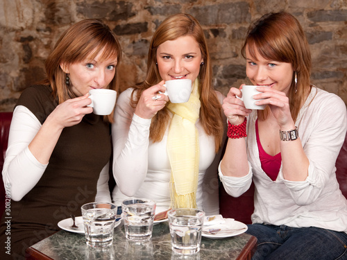 Three beautiful young students waiting drinking  coffee and havi photo