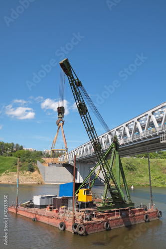 The crane vessel on the river about the bridge