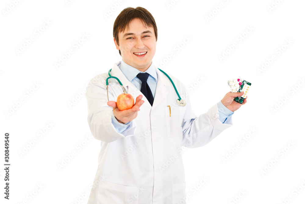 Smiling doctor giving apple and holding pills in other hand Smiling doctor giving apple and holding pills in other hand