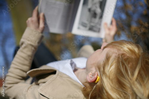 Junge Frau mit Hörgerät liest Zeitung im Wald