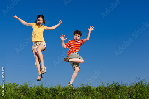 Girl and boy jumping, running against blue sky