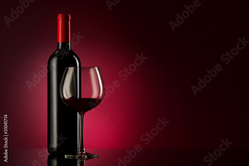 bottle with red wine and glass on a red gradient