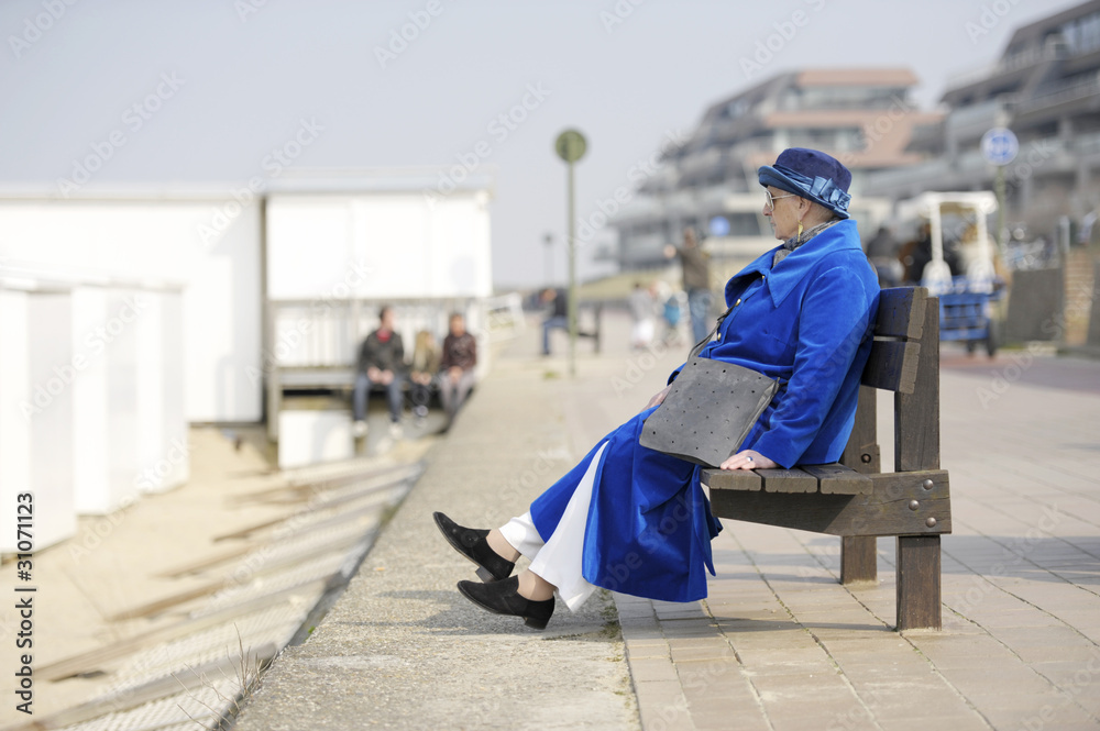 senior woman in electric blue coat and hat sitting on a bench at
