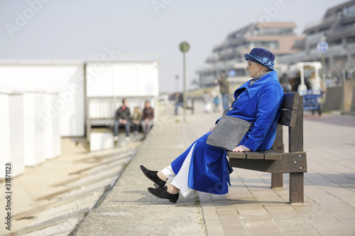senior woman in electric blue coat and hat sitting on a bench at