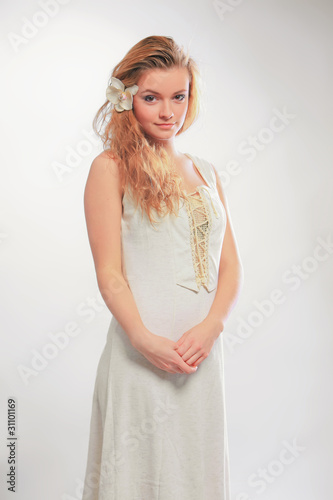 Blonde in a white dress with a flower in her hair with a gray ba