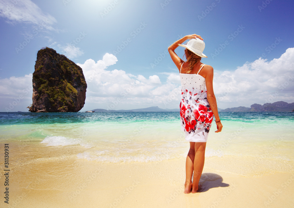 Young woman in summer dress standing on sand and holding straw hat looking to a sky Young woman in summer dress standing on sand and holding straw hat looking to a sky