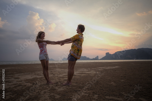 Two young lovers standing on beach and looking to a sun