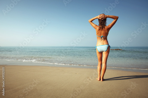 Young woman with wet skin standing on sand and looking to a sea