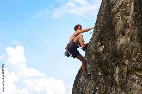 Young male climbing on a cliff on blue cloudy sky background
