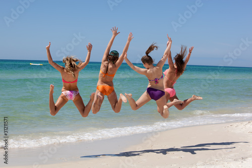 Four Teenage girls jumping on a beach, having fun, arms extended