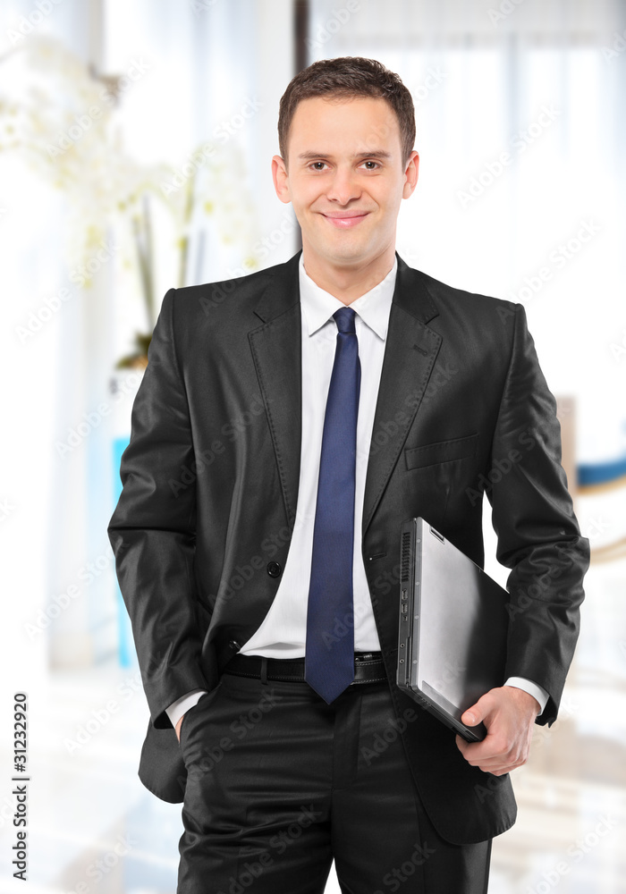 Smiling businessman holding a laptop and posing in his office Smiling businessman holding a laptop and posing in his office